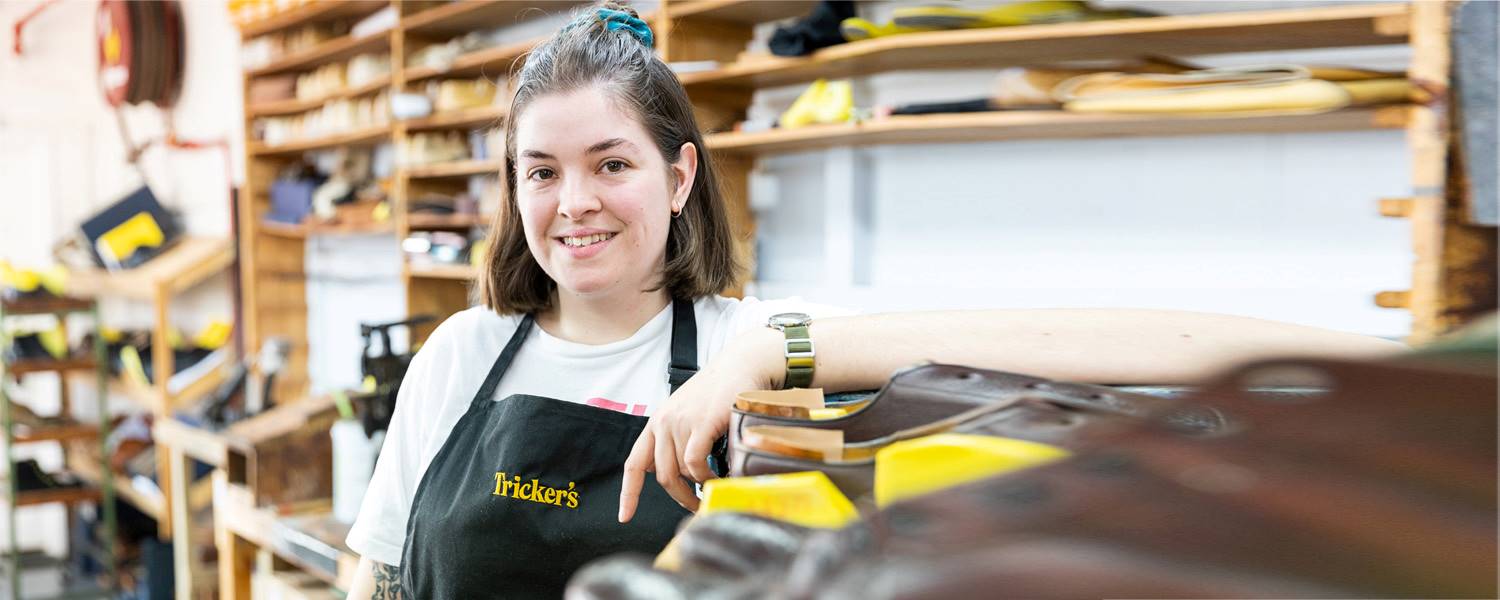 Footwear apprentice in the workshop, posing with her equipment and smiling to camera.